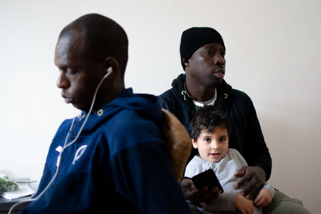 Modou tient l'enfant de son ami dans ses bras pendant qu'il discute