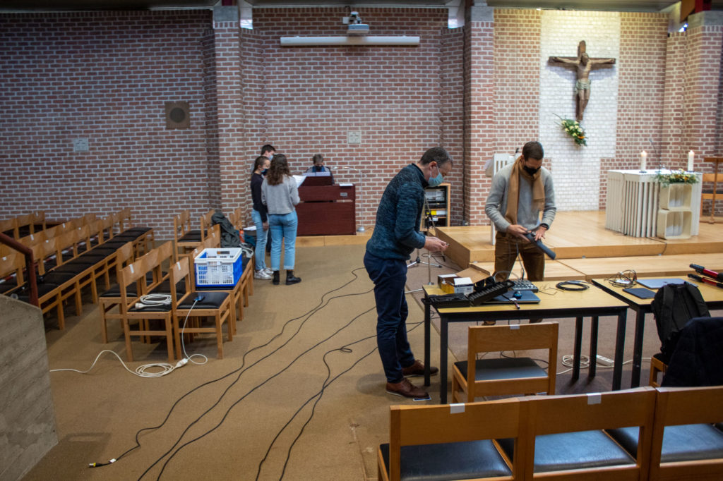 techniciens préparant la régie , déroulant les cables. La chorale répète au fond