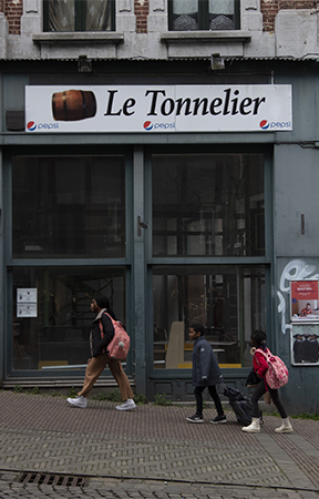 trois passants marchant devant un bar (en faillite) de Charleroi