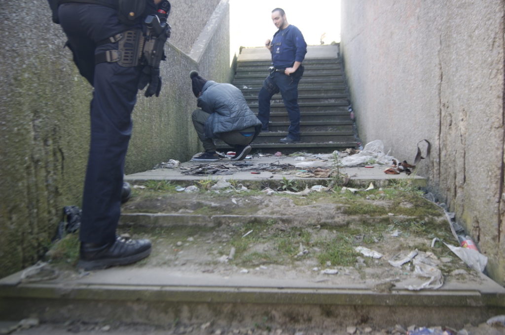 Deux policiers encadrent un homme à genoux qui ramasse son matériel