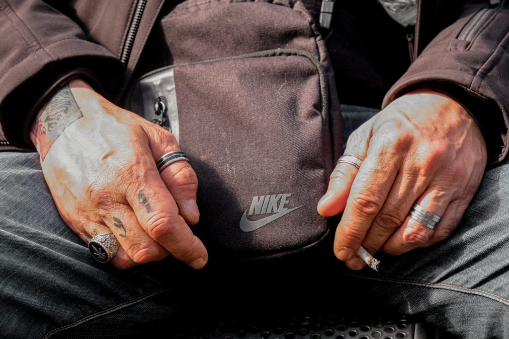 Mains usées d'un sdf, avec sa sacoche Nike et ses bijoux et tatouages