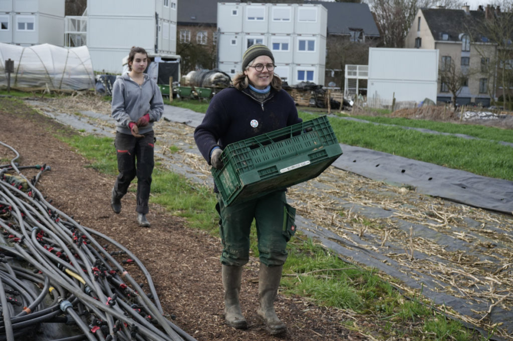 une maraîchère avec un cageot en main et une bénévole derrièreière